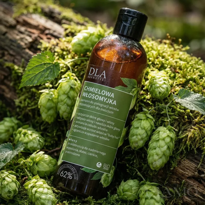 Butelka szamponu Chmielowa Włosomyjka na leśnym mchu w otoczeniu naturalnych szyszek chmielu.