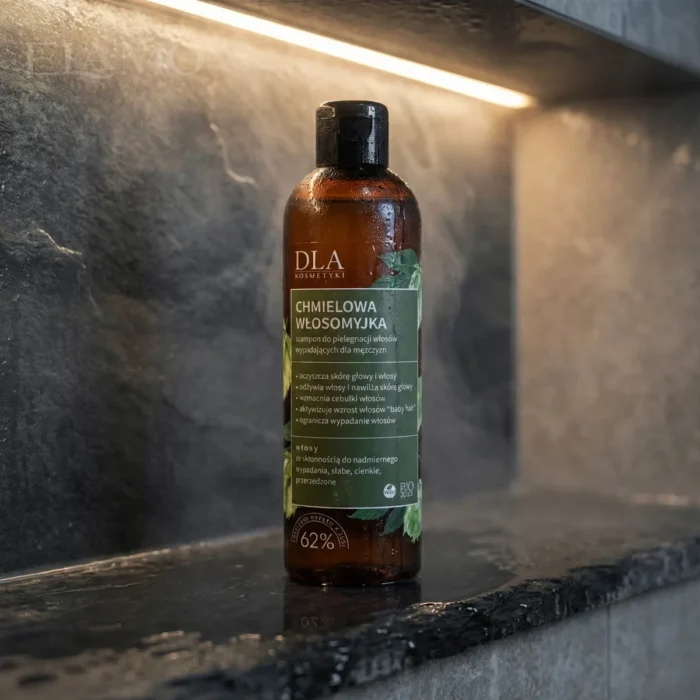 Butelka Chmielowej Włosomyjki stojąca na mokrej kamiennej półce pod prysznicem.