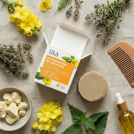 Kompozycja flat lay: Dziewannowa Włosomyjka, drewniany grzebień, masło shea, olej jojoba i zioła na lnianym tle.