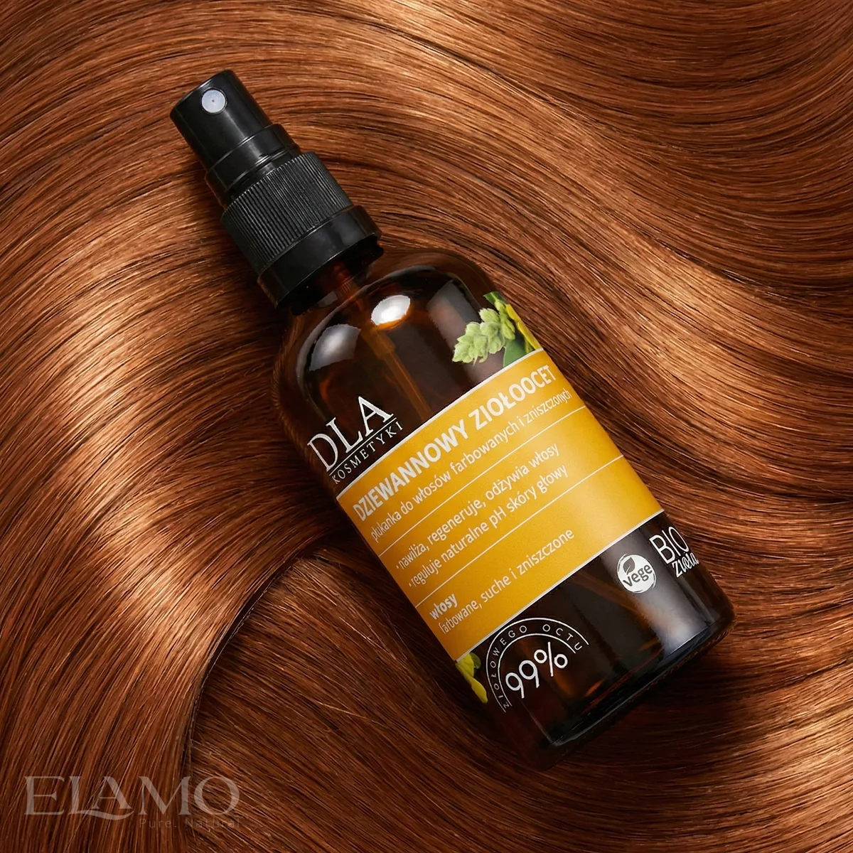 Butelka kosmetyku leżąca na gładkich, lśniących pasmach rudych włosów.