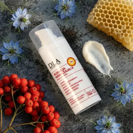 Lekka smuga kremu na dzień, niebieskie kwiaty czarnuszki i plaster miodu na szarym tle