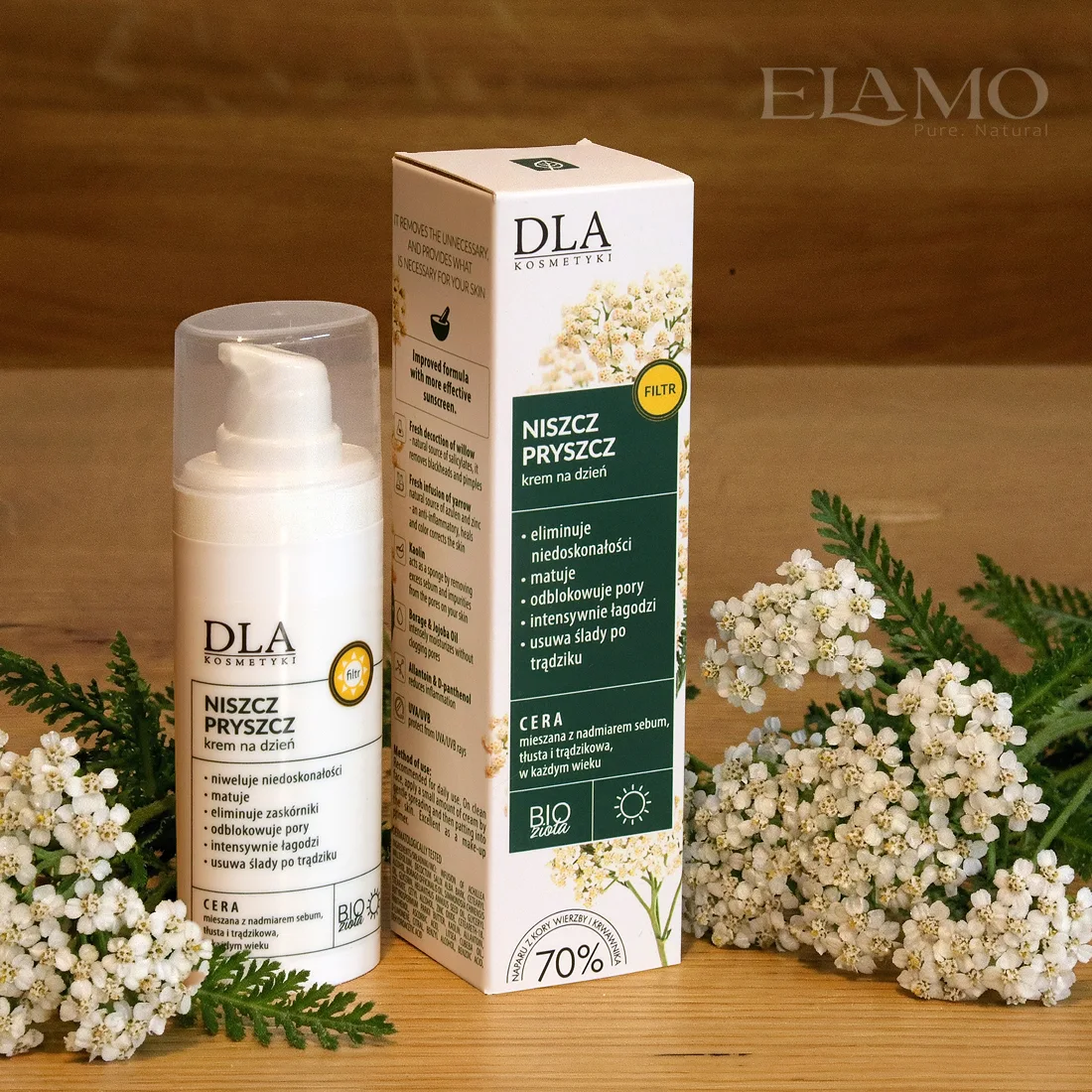 Niszcz Pryszcz krem na dzień – butelka i opakowanie na drewnianym tle, kwiaty krwawnika w aranżacji