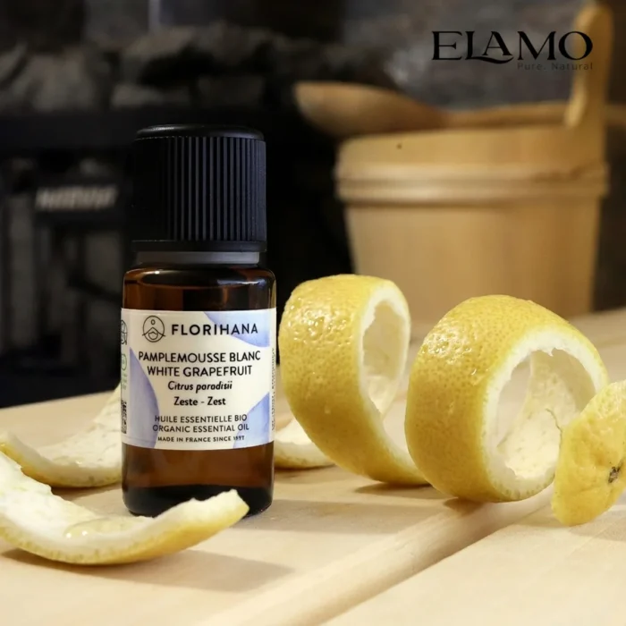 Duży olejek eteryczny z Białego Grejpfruta 15ml Florihana na ławie w saunie, obok spiralnie obciętej skórki cytrusowej.