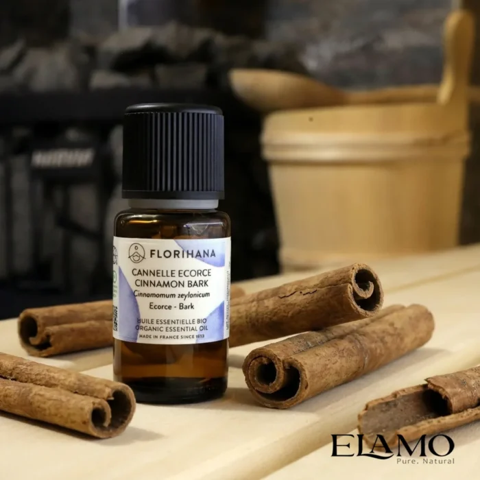 Duży olejek eteryczny z kory cynamonu Florihana 15ml stojący na ławie w saunie pośród lasek cynamonu; silny aromat korzenny.