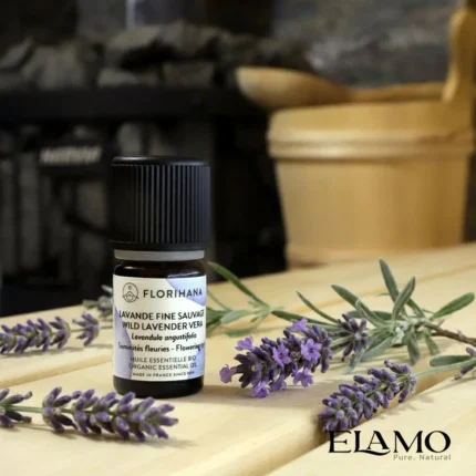 Organiczny olejek eteryczny Lawenda Dzika (Wild Lavender) Florihana stojący na drewnianej ławie w saunie, otoczony świeżymi gałązkami lawendy.