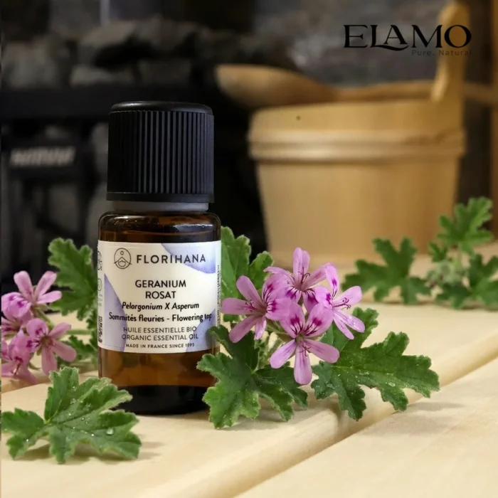 Duży olejek eteryczny Geranium Różane 15ml marki Florihana w scenerii sauny; w tle piec z kamieniami i drewniany ceber.