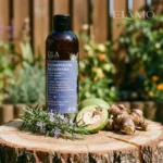 Szampon Rozmarynowa Włosomyjka stojący na drewnianym pniu w ogrodzie obok zielonych orzechów włoskich i korzenia tataraku.