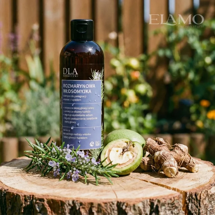 Szampon Rozmarynowa Włosomyjka stojący na drewnianym pniu w ogrodzie obok zielonych orzechów włoskich i korzenia tataraku.