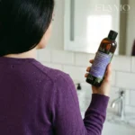 Kobieta w fioletowym swetrze z widocznym łupieżem trzymająca szampon Rozmarynowa Włosomyjka.