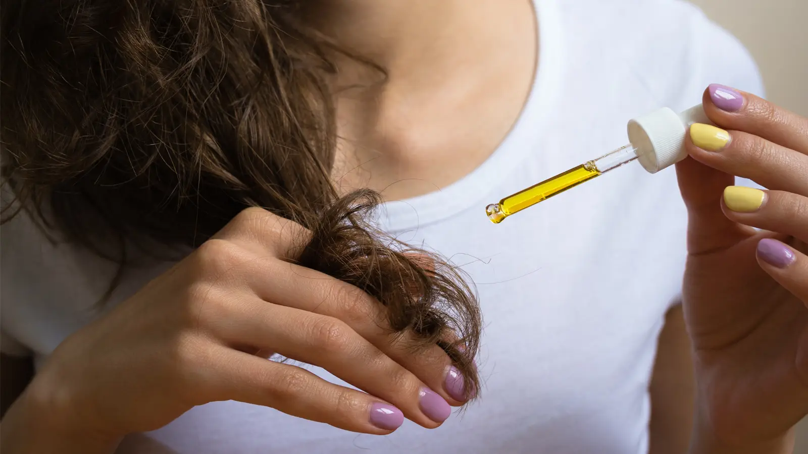 Kobieta aplikuje olej rycynowy z pipety na rozdwojone końcówki włosów, prezentując zabieg pielęgnacyjny.