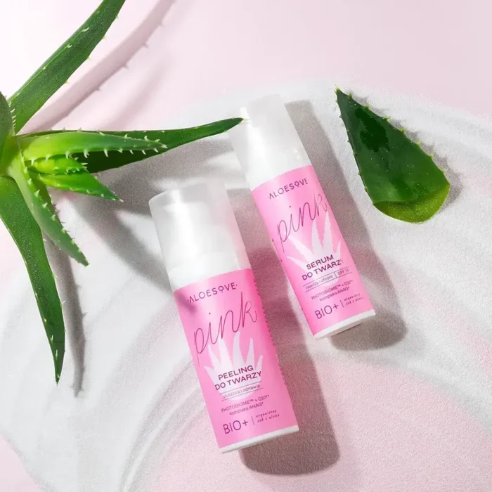 dwa produkty kosmetyczne ALOESOVE Pink: peeling kwasowy do twarzy i serum do twarzy, umieszczone na różowej, satynowej tkaninie. Obok kosmetyków znajduje się świeży, zielony liść aloesu.