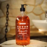 Naturalne mydło marsylskie kwiat pomarańczy w płynie "Fleur d'Orange" marki Bômance, 1 litr, prezentowane na drewnianym stoliku w przytulnej scenerii łazienkowej