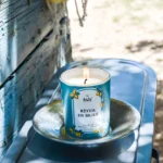 Świeca zapachowa Tadé Méditerranée 'Réveil en Sicile' z cytrusowym aromatem, umieszczona w plenerze na rustykalnym talerzu, tworząca atmosferę sycylijskiego poranka