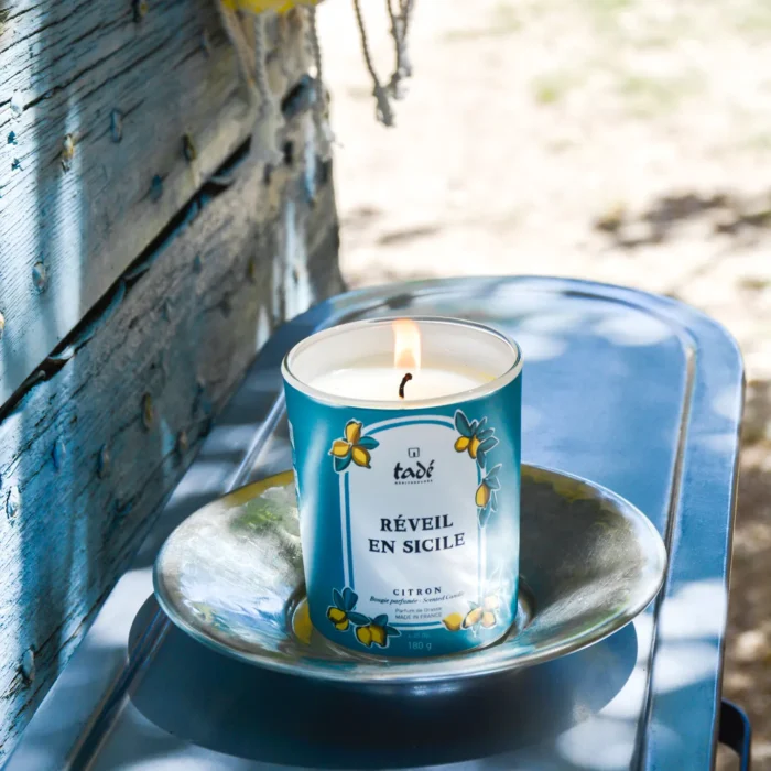 Świeca zapachowa Tadé Méditerranée 'Réveil en Sicile' z cytrusowym aromatem, umieszczona w plenerze na rustykalnym talerzu, tworząca atmosferę sycylijskiego poranka