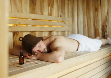 Sauna sucha – mężczyzna leży i odpoczywa na ławie po sesji; obok butelka z kroplomierzem po naturalnym olejku do sauny