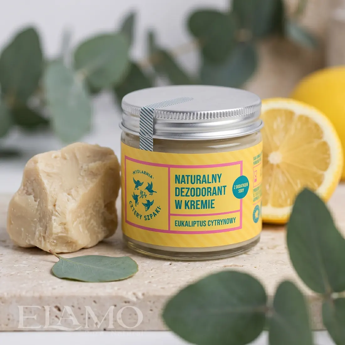 Naturalny dezodorant eukaliptus cytrynowy stojący obok bryłki nierafinowanego masła shea, połówki cytryny i świeżego eukaliptusa.